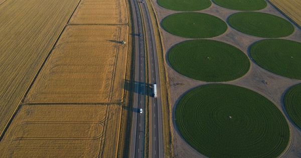 Aerial drone view of a highway crossing between two differently colored farm landscapes